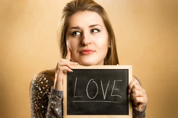 Woman holding blackboard and thinking of love — Stock Photo, Image