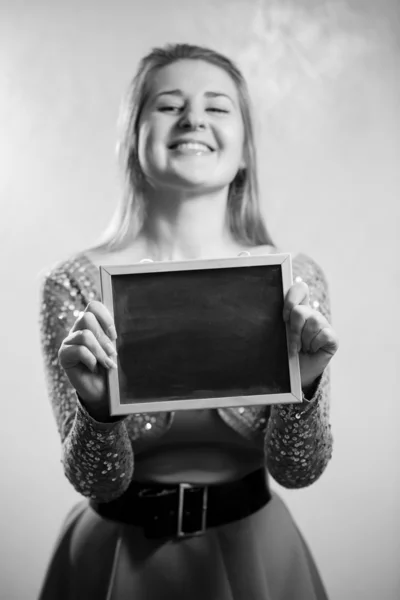 Retrato monocromático de mujer feliz sosteniendo pizarra vacía — Foto de Stock