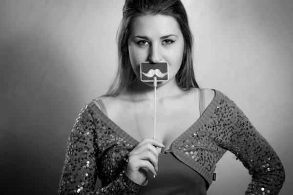 Monochrome portrait of cute woman holding decorative mustache at — Stock Photo, Image