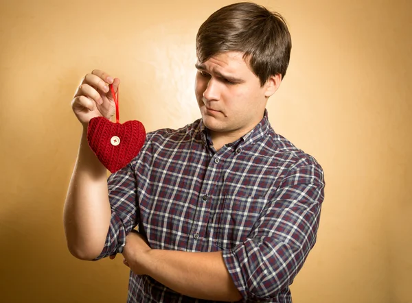 Schöner Mann, der verdächtig auf dekoratives rotes Herz blickt — Stockfoto