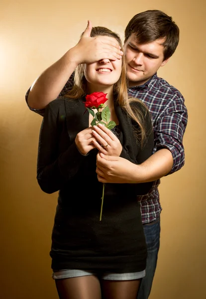 Giovane uomo chiusura fidanzate occhi e dando la sua rosa rossa — Foto Stock