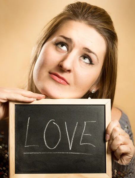 Thoughtful woman holding word "Love" written on blackboard — Stock Photo, Image