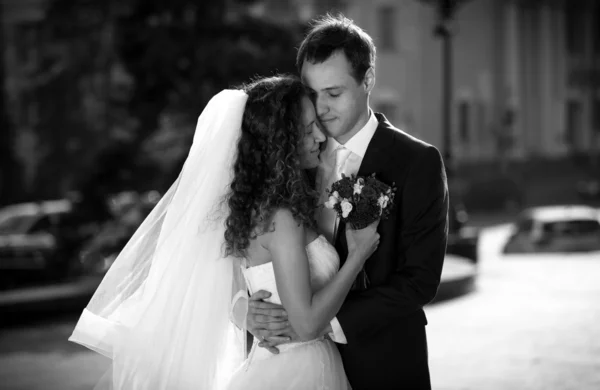 Monochrome portrait of embracing bride and groom on street — Stock Photo, Image