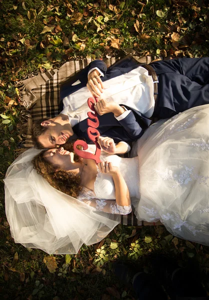 Nevěsta a ženich ležící na trávě a drží, "Love" podepsat — Stock fotografie