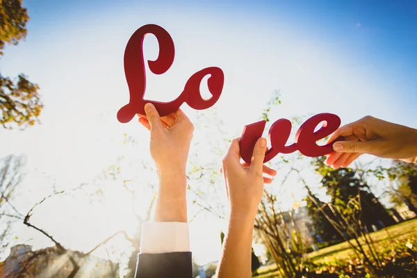 Conceptual photo of man and woman holding halves of "Love" sign — Stock Photo, Image