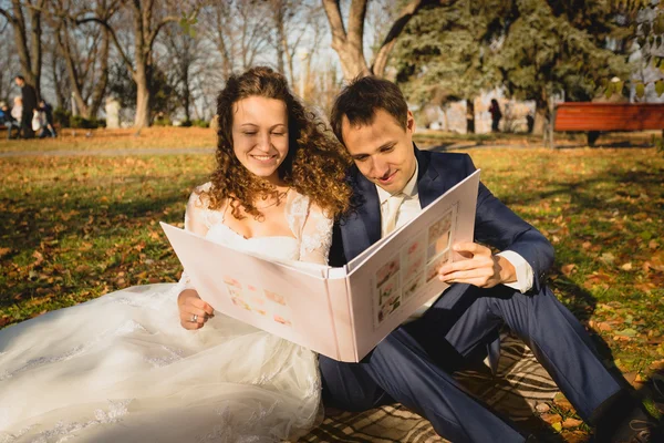 Просто женатая пара, сидящая на траве в парке и смотрящая фотографии — стоковое фото