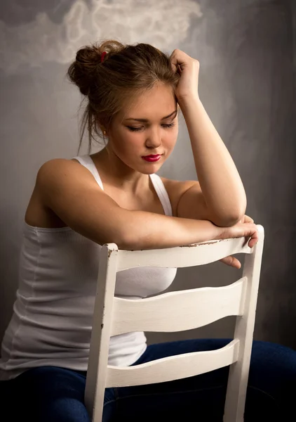 Portrait of thoughtful blonde woman sitting on white wooden chai — Stock Photo, Image