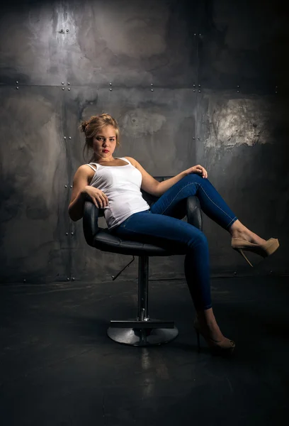 Séduisante femme assise sur une chaise dans une chambre sombre grungy — Photo