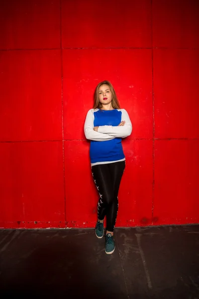 Stijlvolle vrouw in hoodie en beenkappen leunend tegen rode muur — Stockfoto