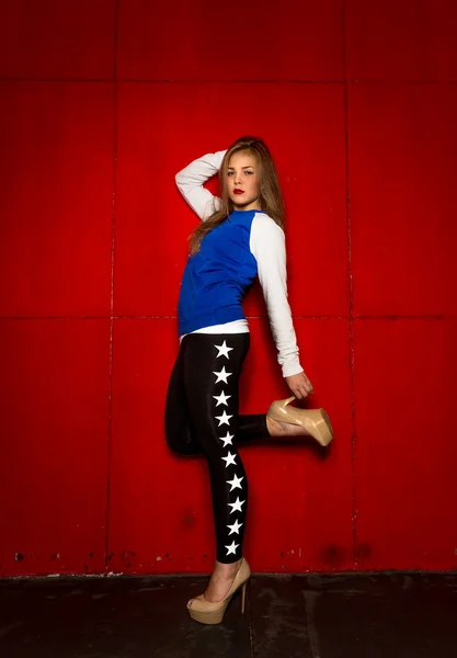 Blonde girl in legging and high heels posing against red wall — Stock Photo, Image