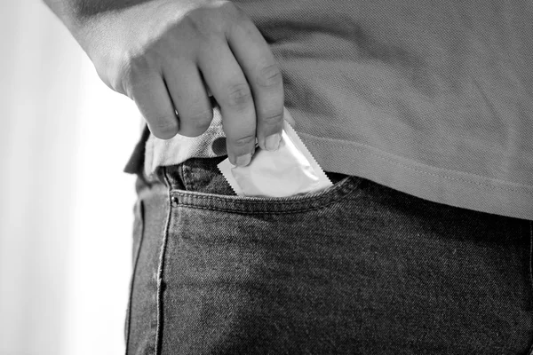 黑色和白色拍摄的人把避孕套放在牛仔裤的口袋里 — 图库照片