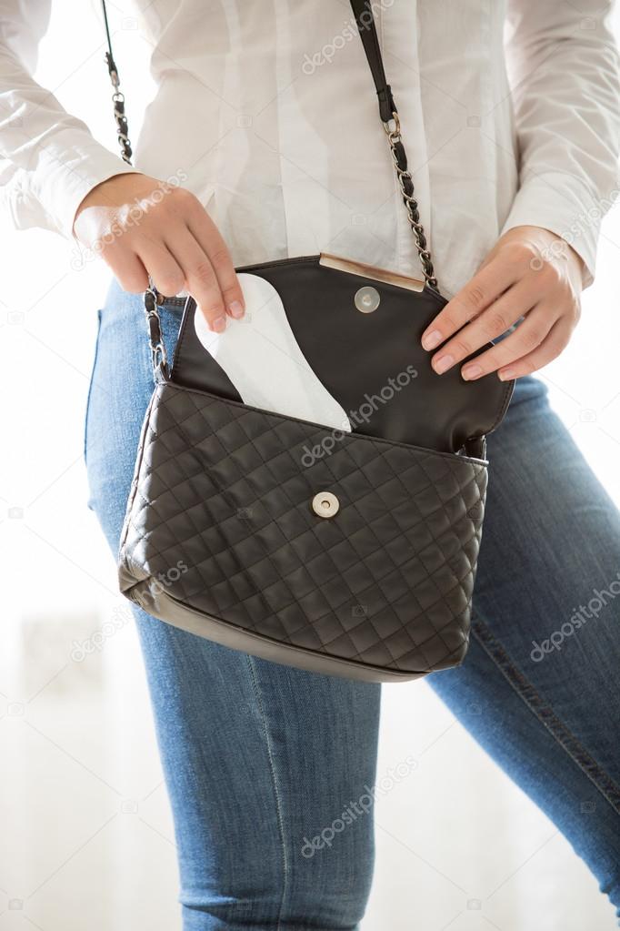 young stylish woman putting hygiene pad in handbag