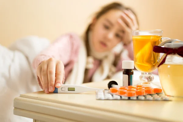 Portrait of sick girl lying in bed and taking thermometer from t — Stock Photo, Image