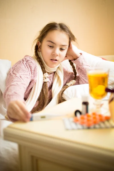 Portrait of little sick girl lying in bed and looking at thermom — Stock Photo, Image