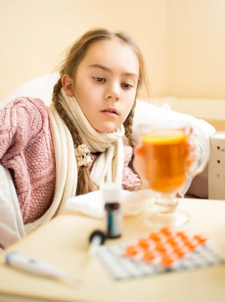 Petite fille avec la grippe couchée dans le lit et regardant une tasse de thé — Photo