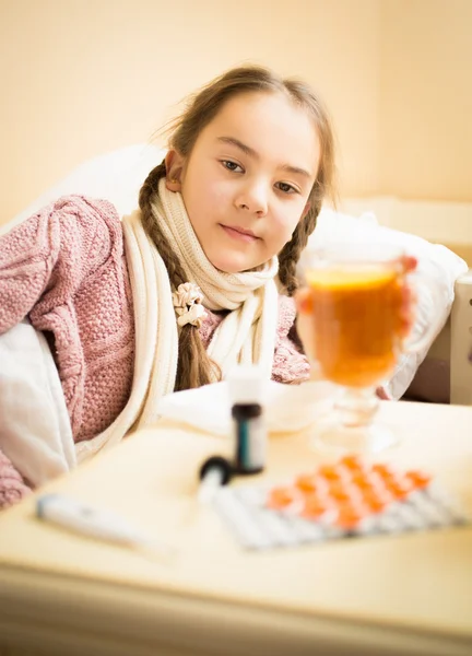 Little sick girl lying in bed taking cup of tea with lemon — Stock Photo, Image