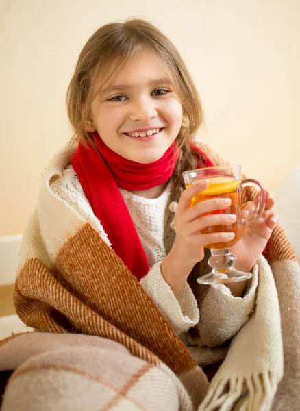 Sorridente ragazza in sciarpa ricoperta di plaid contenente tazza di tè caldo — Foto Stock