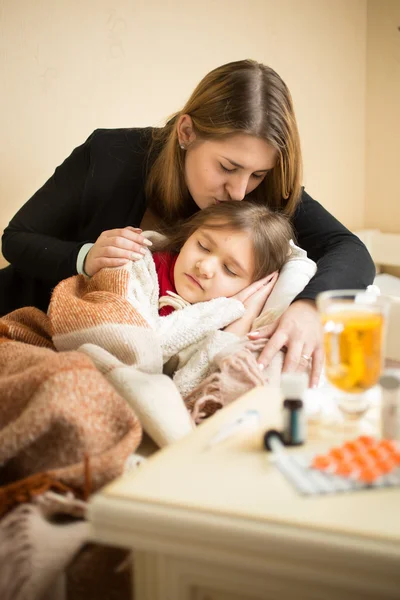 Mladá starostlivá matka líbání v hlavě dcera nemocná v posteli — Stock fotografie