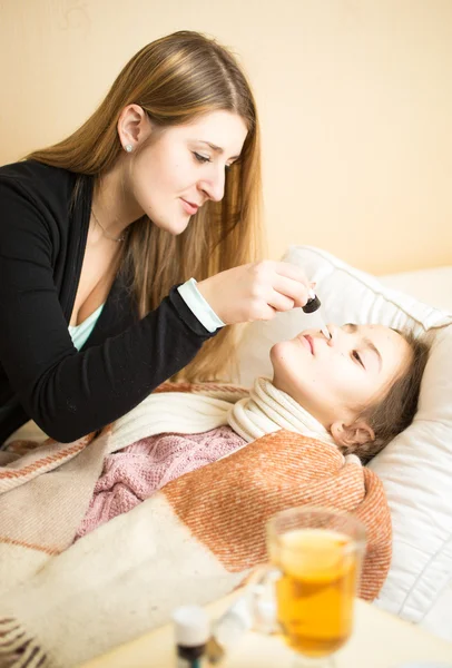 Mère attentionnée pulvérisation filles nez couché dans le lit — Photo