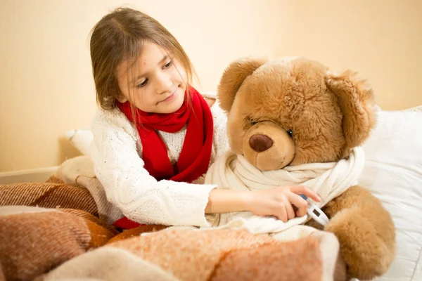 Chica acostada en la cama y midiendo la temperatura de los osos de peluche con el — Foto de Stock