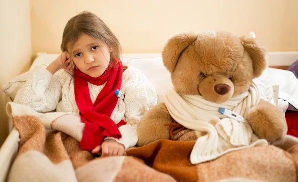 Chica triste medición de temperatura con osito de peluche en la cama — Foto de Stock