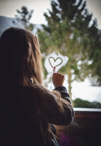 Portrait of little girl drawing heart on frozen window — Stock Photo, Image