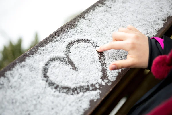 Kleines Mädchen zeichnet Herz auf Schnee — Stockfoto