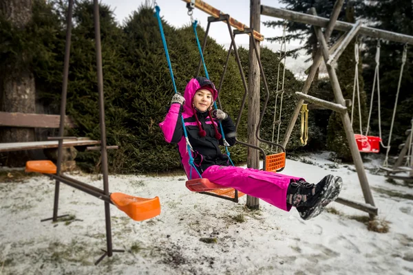 Smiling girl riding on swing on playground at snowy day — Stock Photo, Image