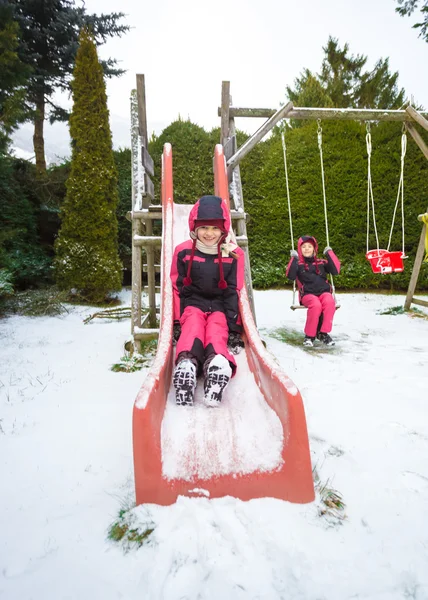 Lachende meisje rijden naar beneden de dia op Speeltuin bedekt met sn — Stockfoto