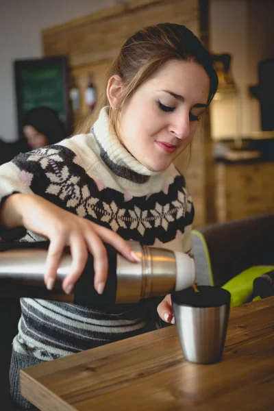 Portræt af kvinde i trøje hælde kaffe fra termokande i kop - Stock-foto