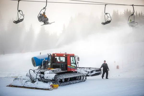 Máquina de limpeza de neve trabalhando na pista de esqui sob cadeiras de cabo — Fotografia de Stock