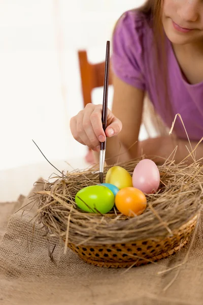 Girl holding paintbrush and coloring Easter eggs — Stock Photo, Image