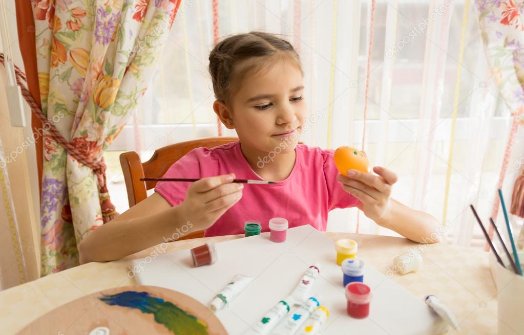 girl painting Easter eggs at table on kitchen