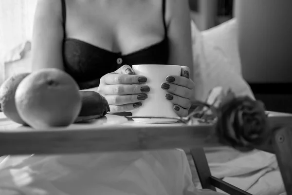 Black and white photo of woman drinking coffee in bed — Stock Photo, Image