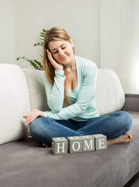 Beautiful woman sitting on sofa and looking on word "home" — Stock Photo, Image