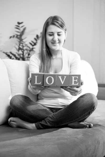 Black and white photo of woman on couch and holding word "love" — Stock Photo, Image