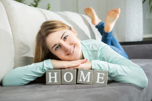 Lachende vrouw liggen op woord "thuis" gespeld door letters op bakstenen — Stockfoto