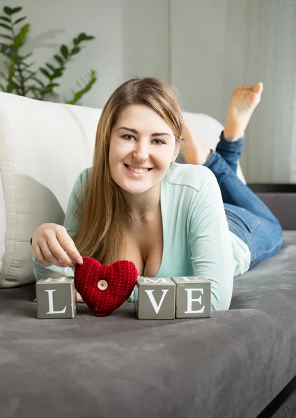 Happy woman lying on sofa at room and holding word "love" — Stock Photo, Image