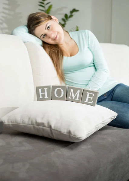 Woman sitting on sofa and looking on word "Home" spelled by wood — Stock Photo, Image