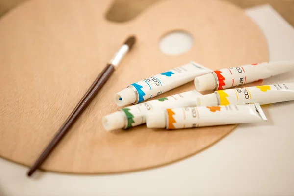 Macro shot of oil paint tubes an paintbrush lying on pallet — Stock Photo, Image