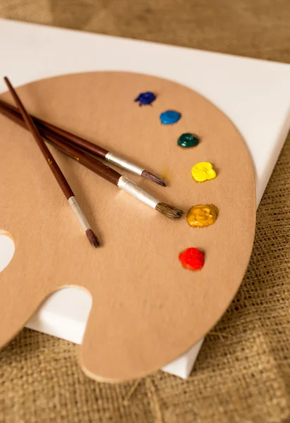 Paintbrushes lying on wooden pallet with oil paint blobs — Stock Photo, Image