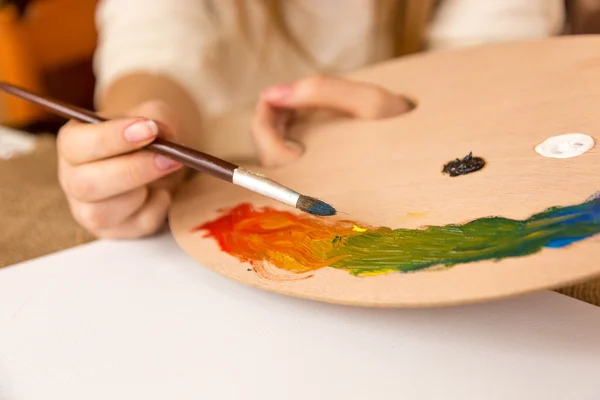 Woman holding paintbrush and choosing paint on pallet — Stock Photo, Image