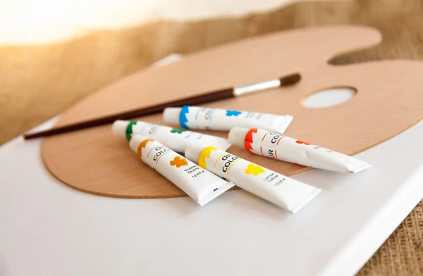 Oil paints in tubes and paintbrush lying on wooden pallet — Stock Photo, Image