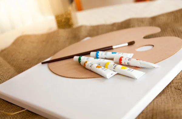 Tubos de pintura, paleta y pincel acostados en la mesa en la sala de estar —  Fotos de Stock