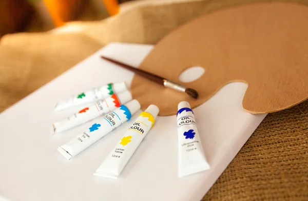 Paleta y tubos de pintura al óleo acostado sobre lienzo blanco —  Fotos de Stock
