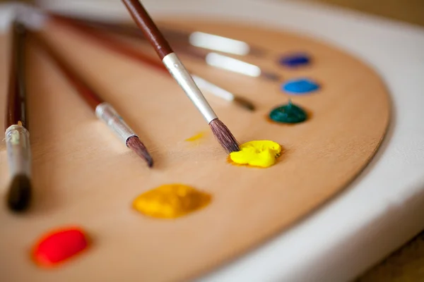 Paints on wooden pallet. Focus on paintbrush dipped in yellow pa — Stock Photo, Image