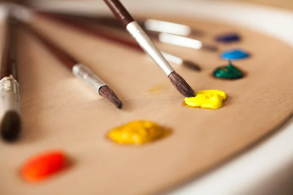 Macro photo of paintbrush dipped in yellow oil paint from pallet — Stock Photo, Image