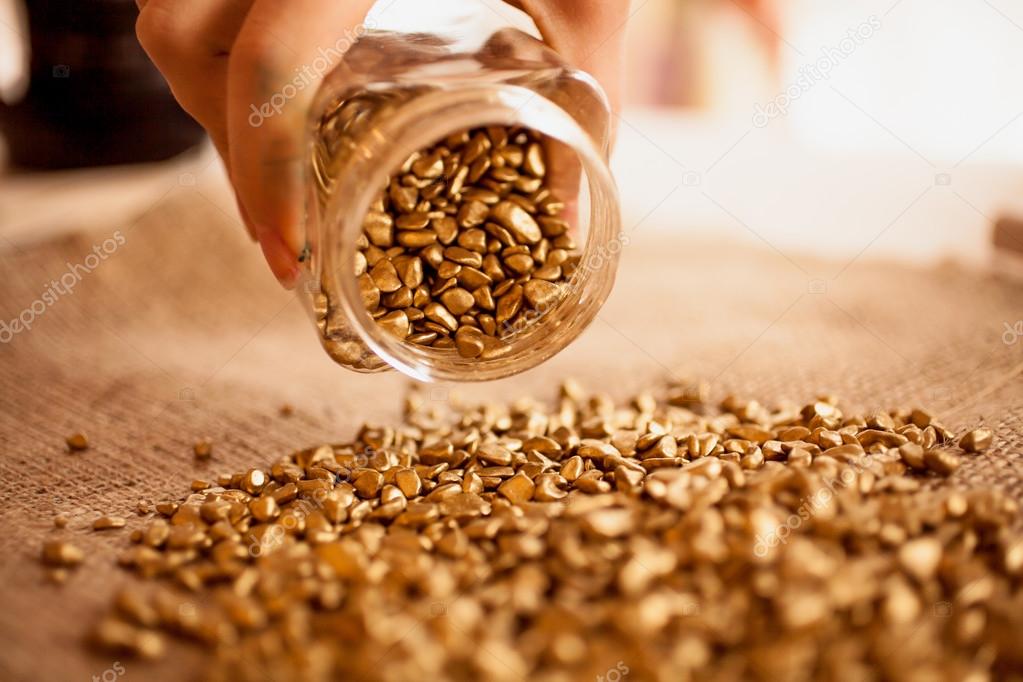 Closeup photo of man pouring out jar full of golden nuggets