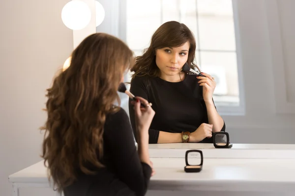 Hermosa morena sentada en el espejo y haciendo maquillaje —  Fotos de Stock