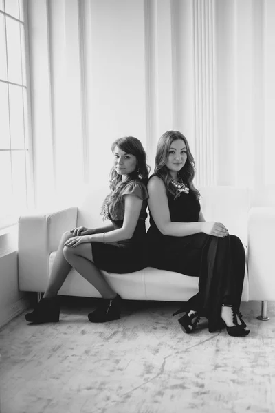 Black and white photo of two woman sitting back to back on couch — Stock Photo, Image